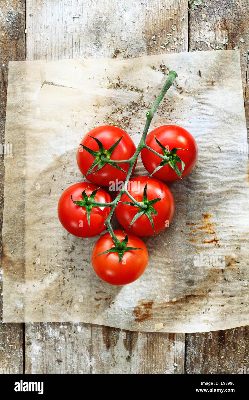 Bunch of fresh red tomatoes in grungy kitchen on a piece of stained, wrinkled oily oven paper on an old wooden tabletop Stock Photo