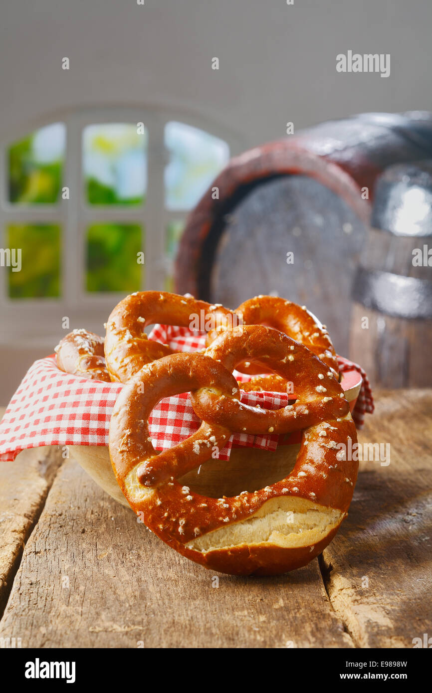 Crisp golden knot-shaped pretzels on a wooden table with an old vintage oak barrel and summery window behind Stock Photo