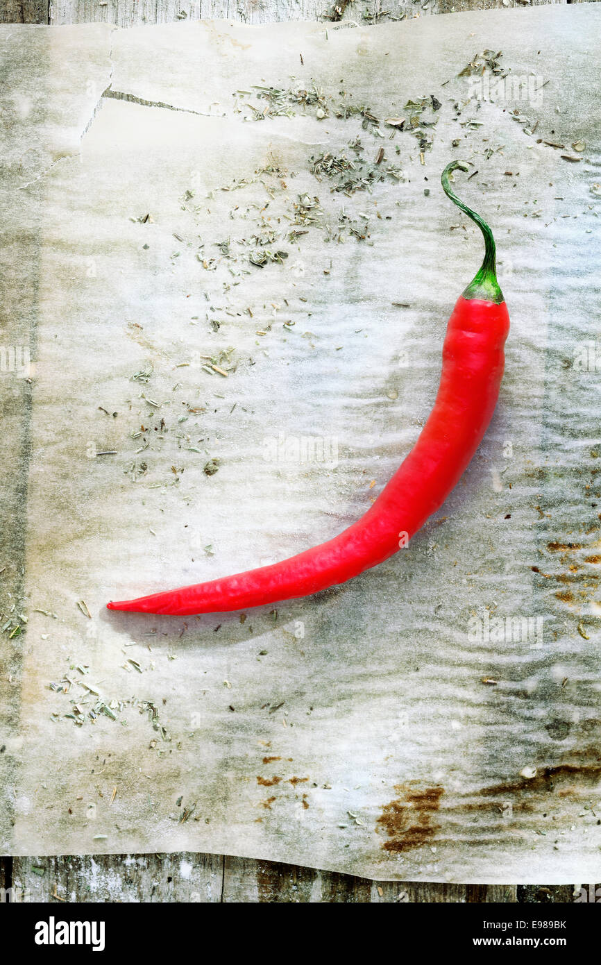 Single hot chili on grungy soiled paper in a kitchen on a rustic wooden table Stock Photo