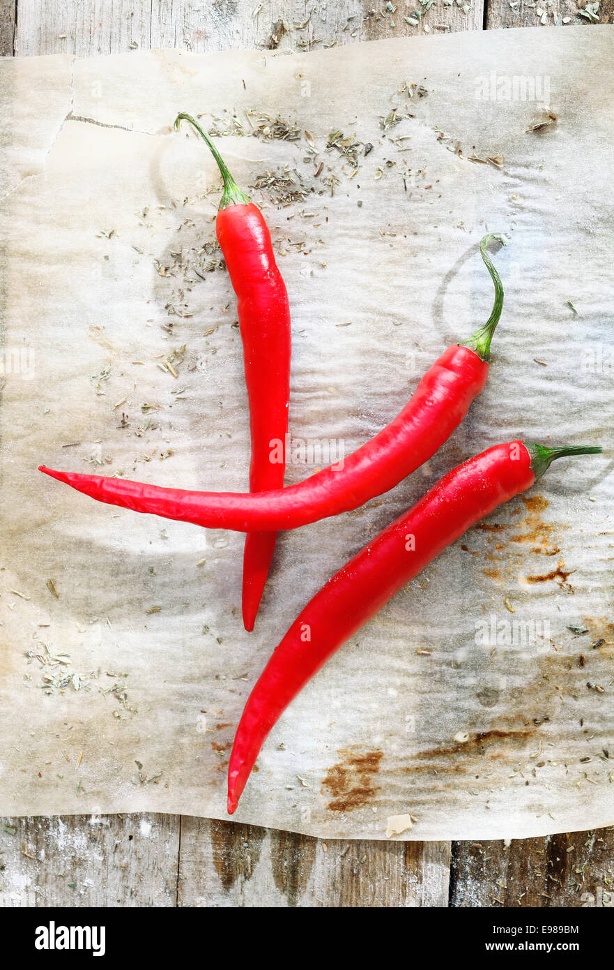 Red chilli peppers on a sheet of grunge used oven paper on a rustic wooden table Stock Photo