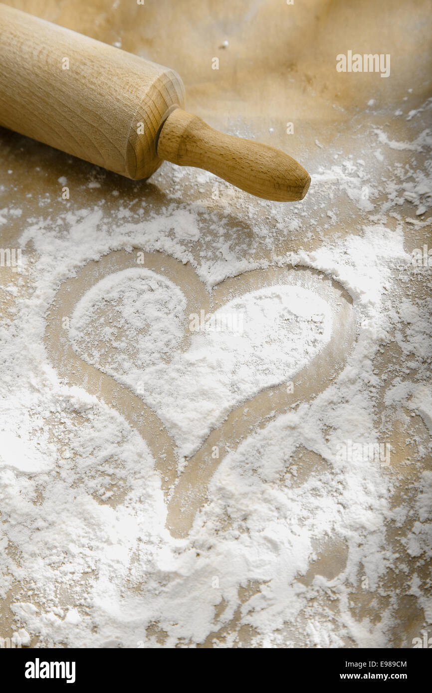 Hand drawn heart in sprinkled flour with a wooden rolling pin showing a love and enjoyment of cooking and baking Stock Photo