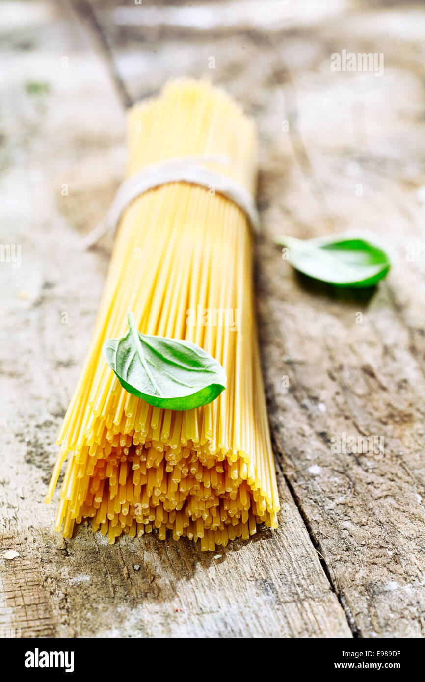 Bundle of uncooked spaghetti with basil for use in the kitchen to prepare fresh Italian pasta dishes Stock Photo