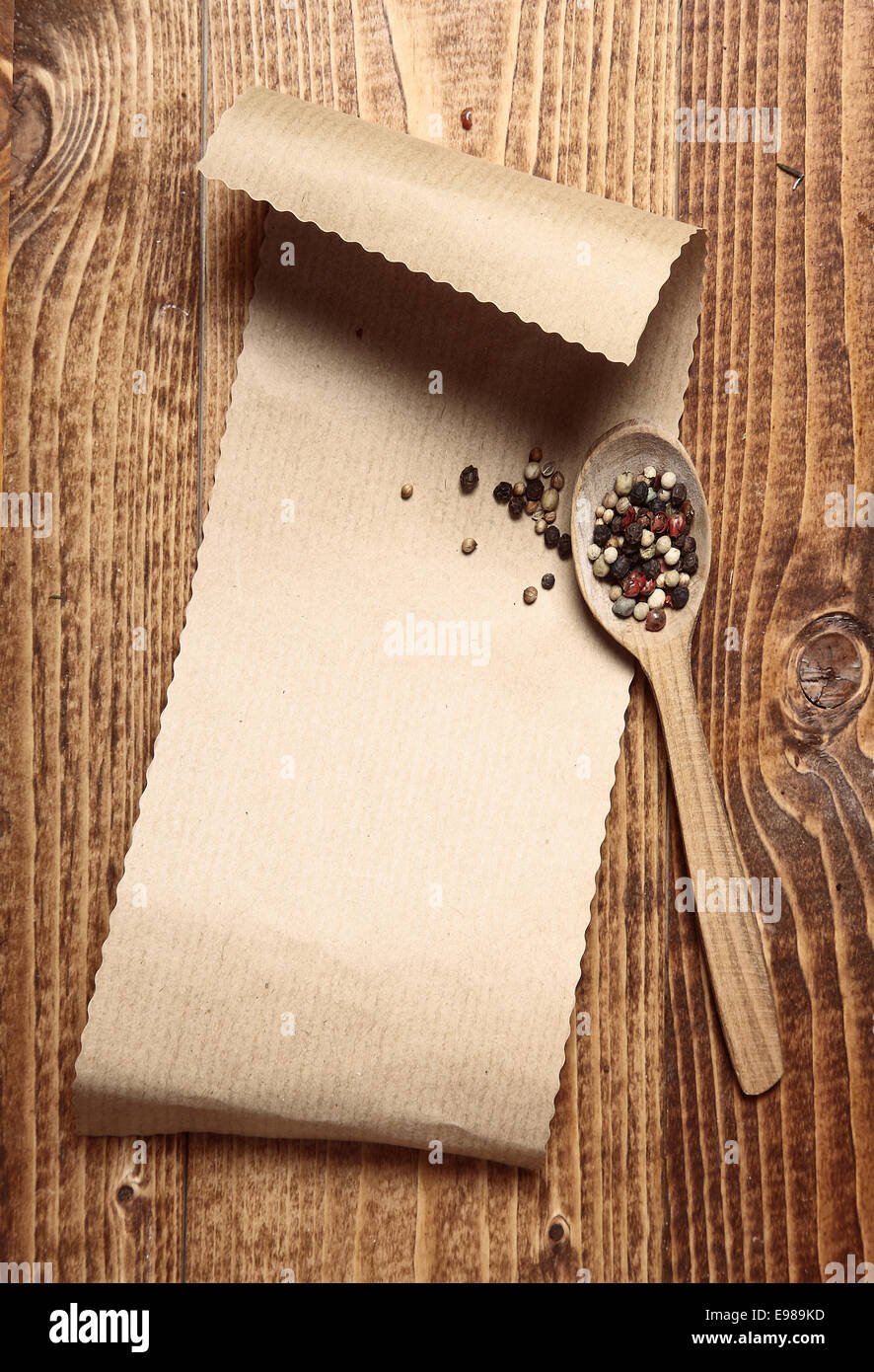 Brown paper on wood with a wooden spoon and peppercorns Stock Photo