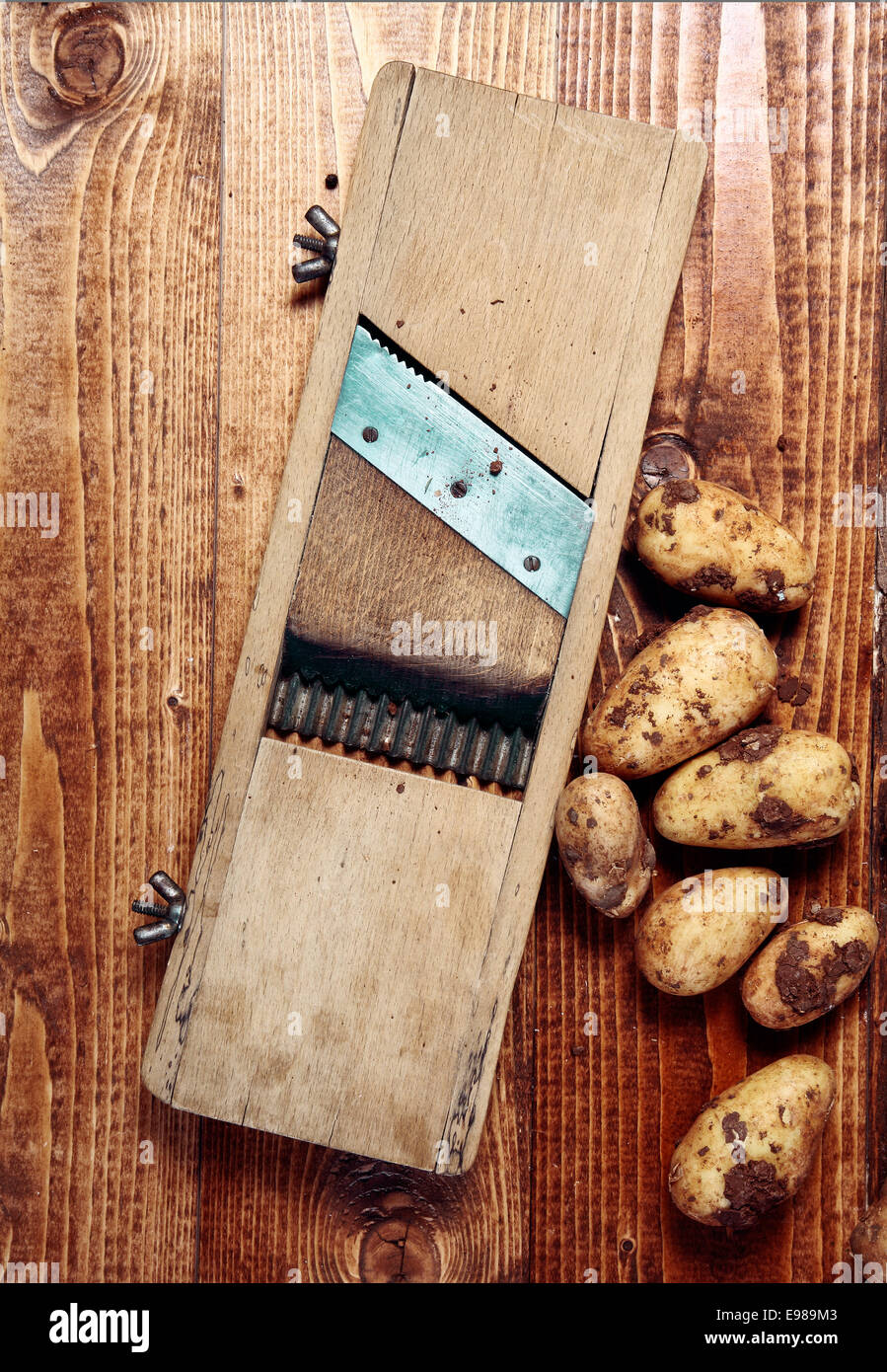 Old vintage wooden chip maker with an adjustable blade alongside fresh farm potatoes, overhead view on a wooden kitchen table Stock Photo