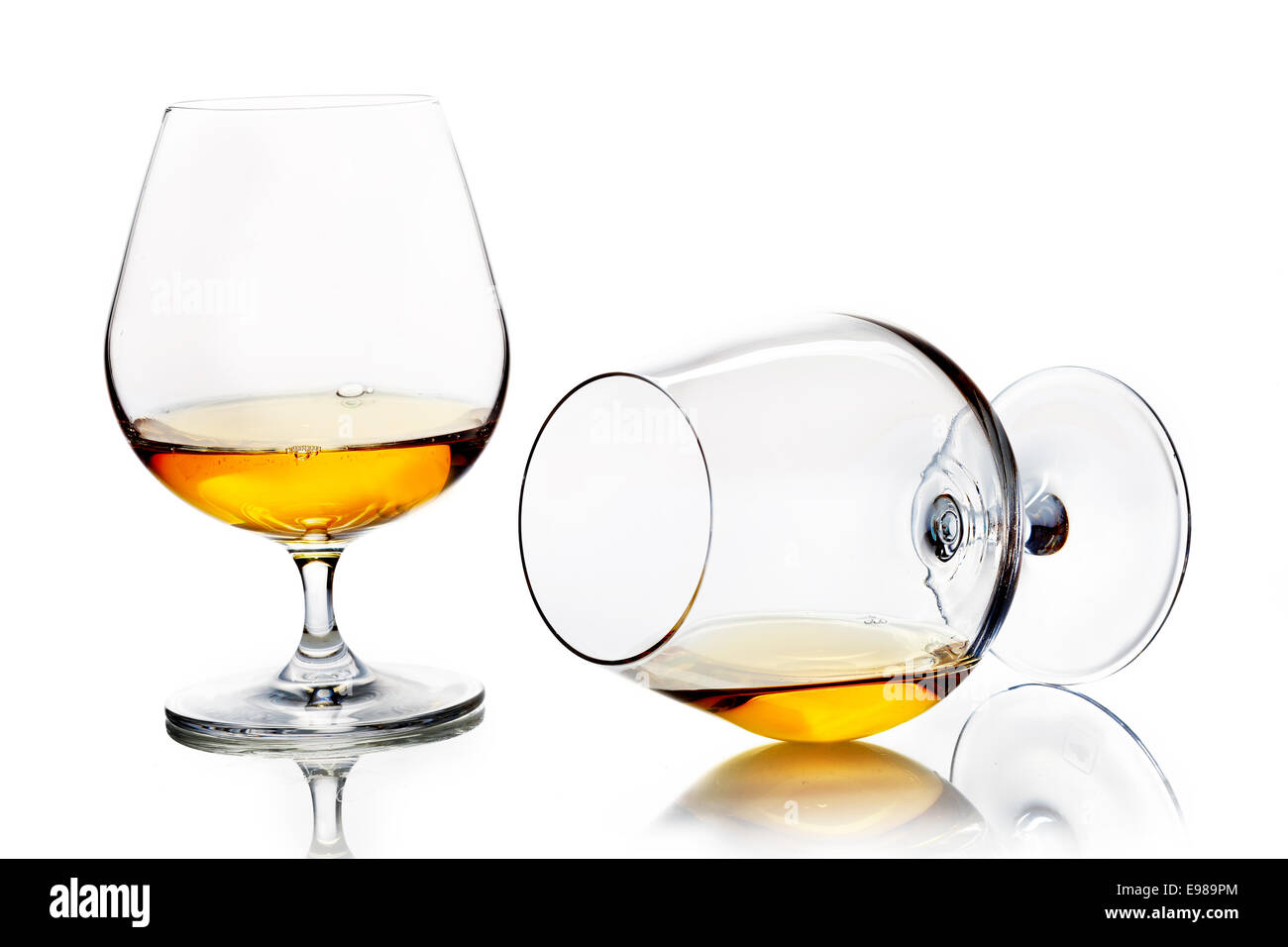 Snifters with brandy or cognac, one standing upright and one angled towards the camera lying on its side on a white studio background Stock Photo