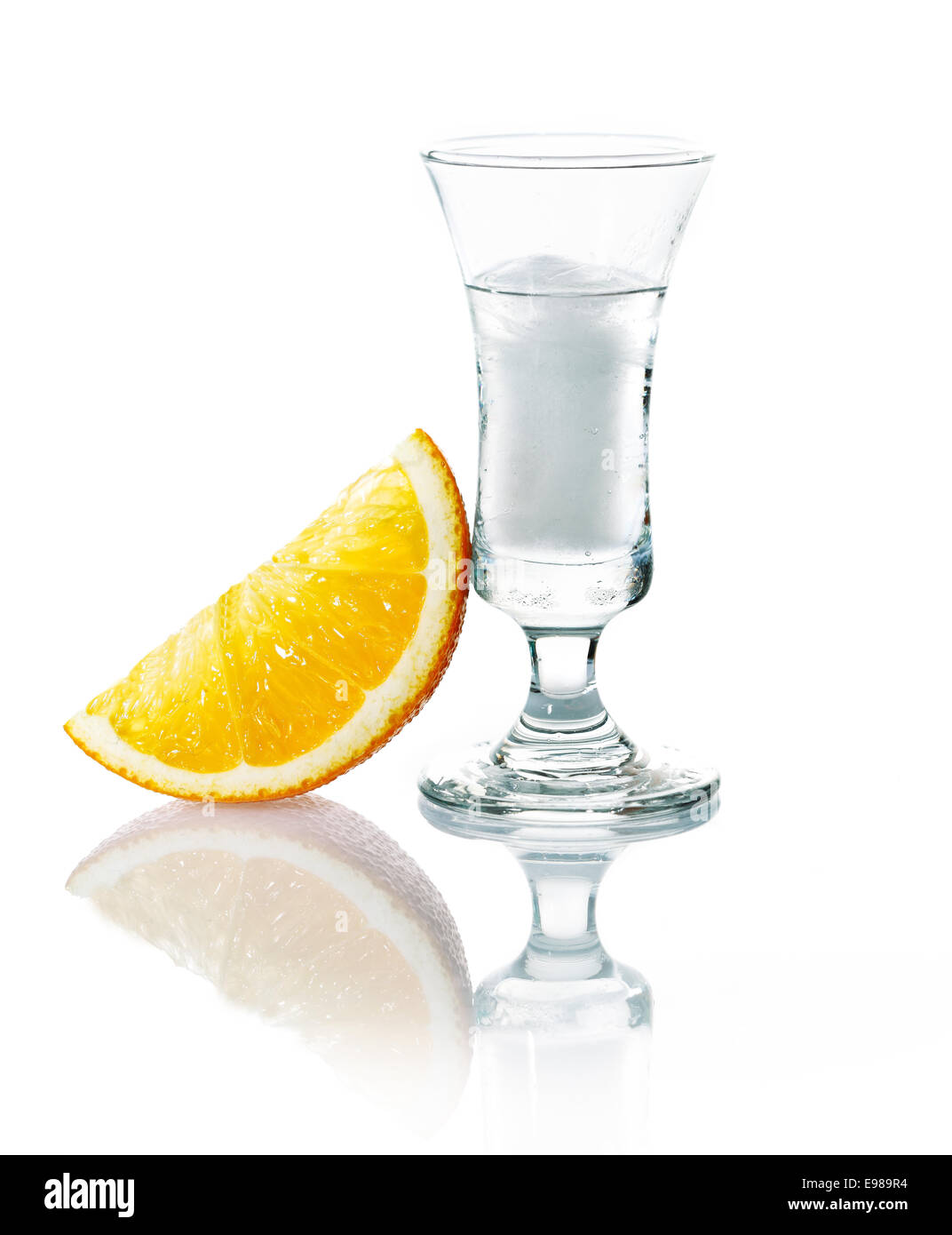 Shot glass with vodka or gin on the rocks served with a slice of fresh orange on a white studio background with reflection Stock Photo