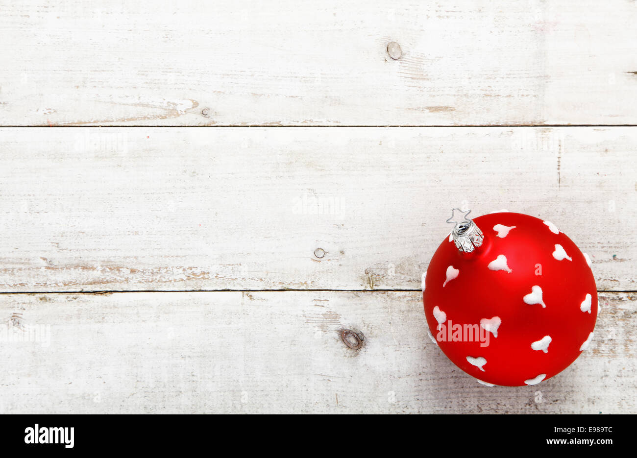 A vivid red bauble dotted with white hearts suitable as a Christmas or Valentines decoration on a background of white wooden boards with copyspace Stock Photo