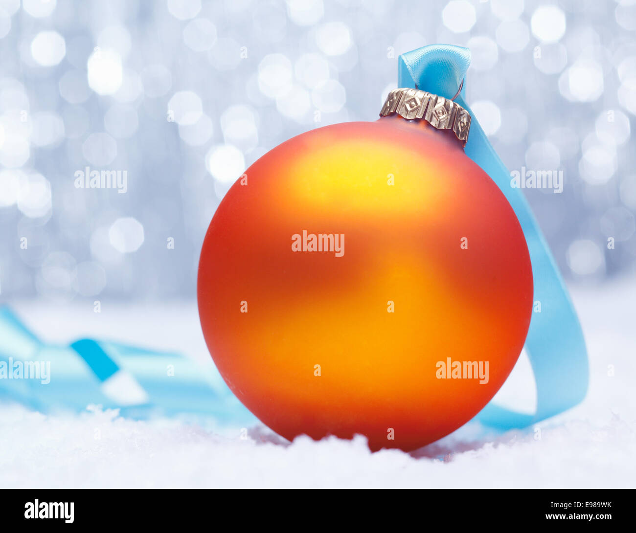 Glowing golden orange Christmas bauble nestled on fresh winter snow with a backdrop of sparkling festive lights Stock Photo