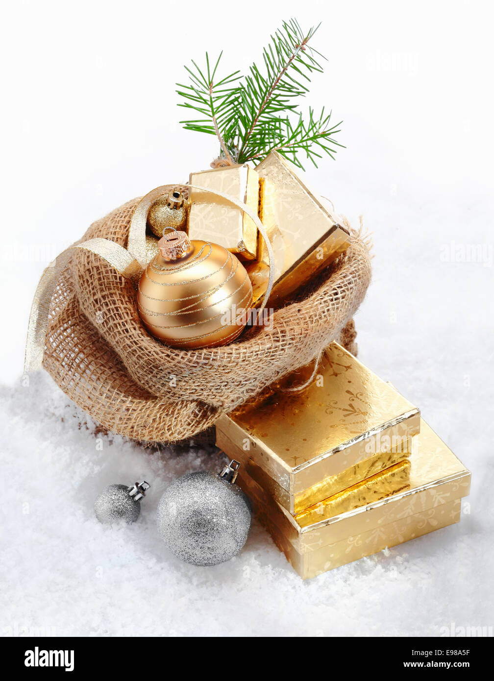 Gold Christmas gifts for a country celebration overflowing a simple hessian sack decorated with a bauble and pine needles nestled in fresh winter snow Stock Photo