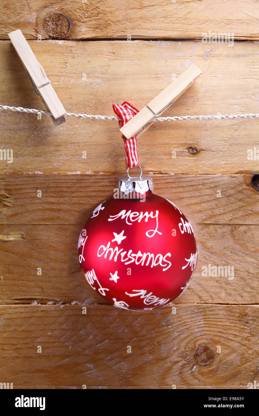 Colourful red merry Christmas bauble with a written greeting hanging from a line by a clothespeg over rustic rough wooden boards Stock Photo