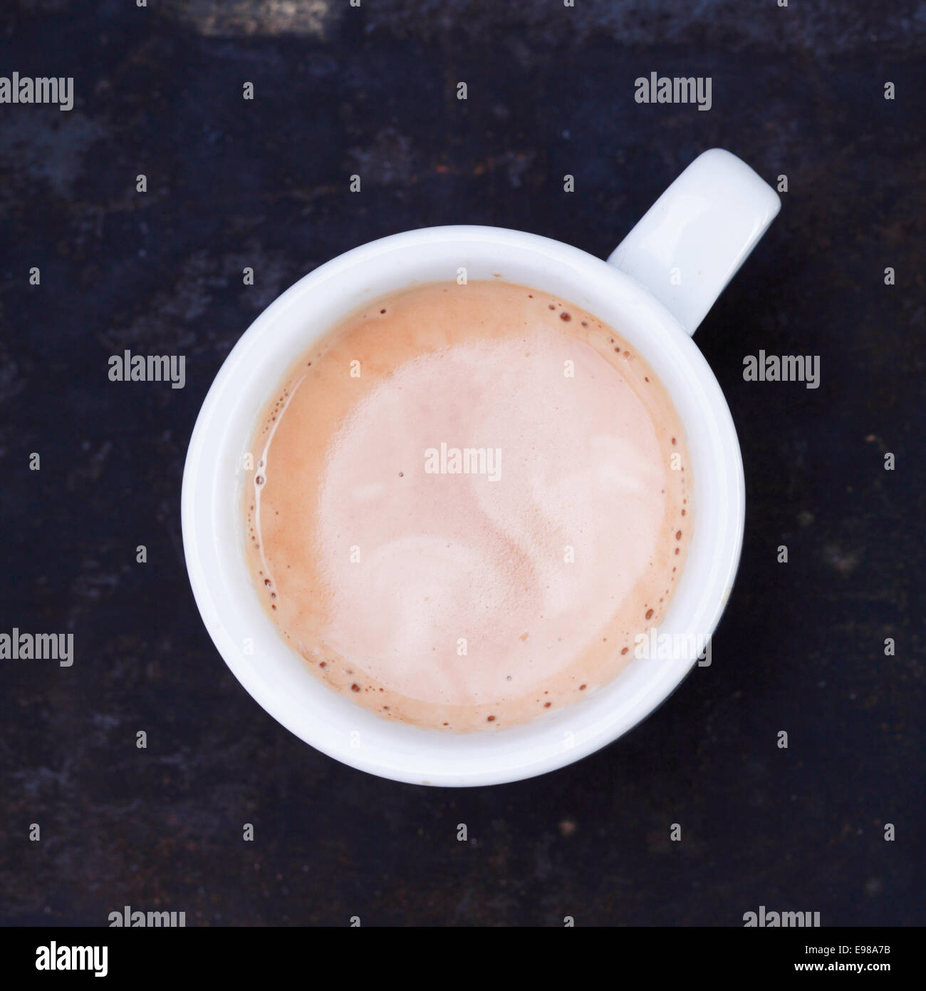 Overhead view of a hot frothy cup of cappuccino or cafe au lait standing on a slate blackboard in square format Stock Photo