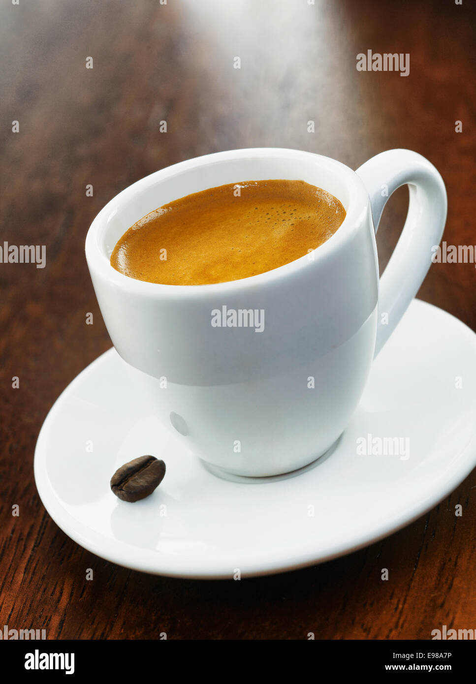 A full white coffee cup with a single coffee bean on the saucer, on a dark wood background Stock Photo
