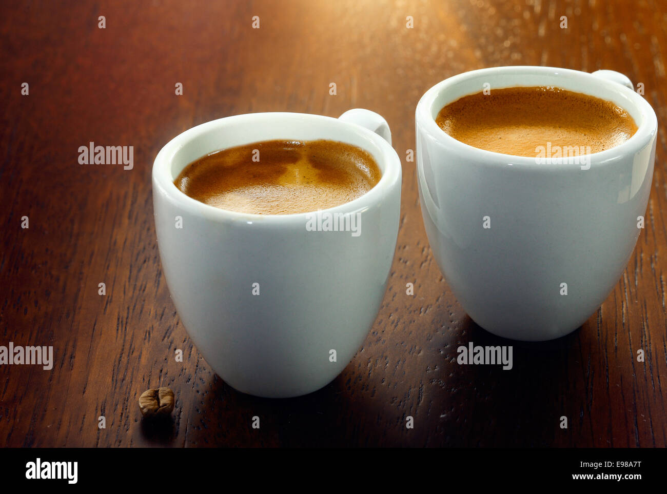 Two espresso coffees in small white cups,with a single coffee bean resting on the wood background Stock Photo