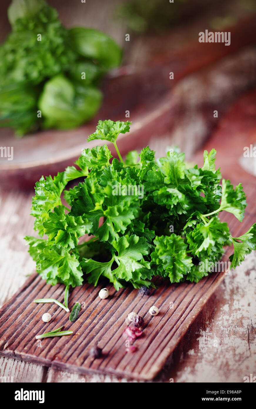 Bunch of fresh crinkly leafed parsley lying on a rustic wooden chopping board on a grunge wooden kitchen table Stock Photo