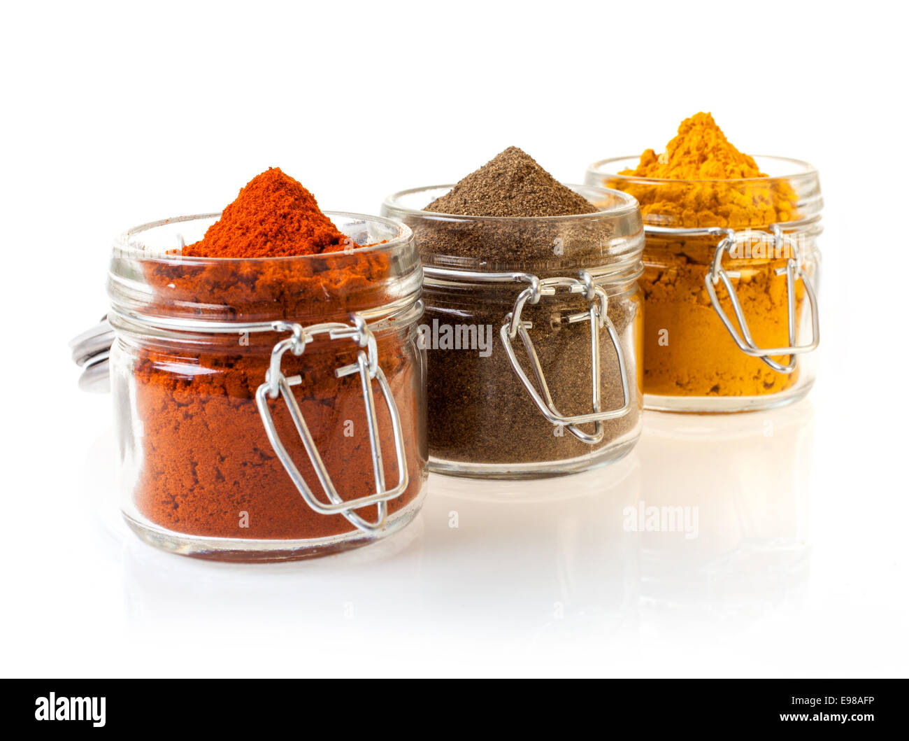 Three glass jars filled with colourful ground spices including chilli, curry and cinnamon, on a white background Stock Photo