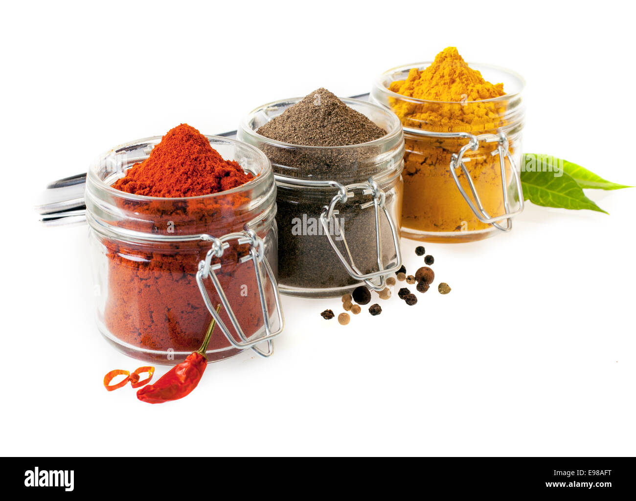 Three glass containers filled with ground culinary spices with chilli peppers, black peppercorns and curry powder on a white background Stock Photo