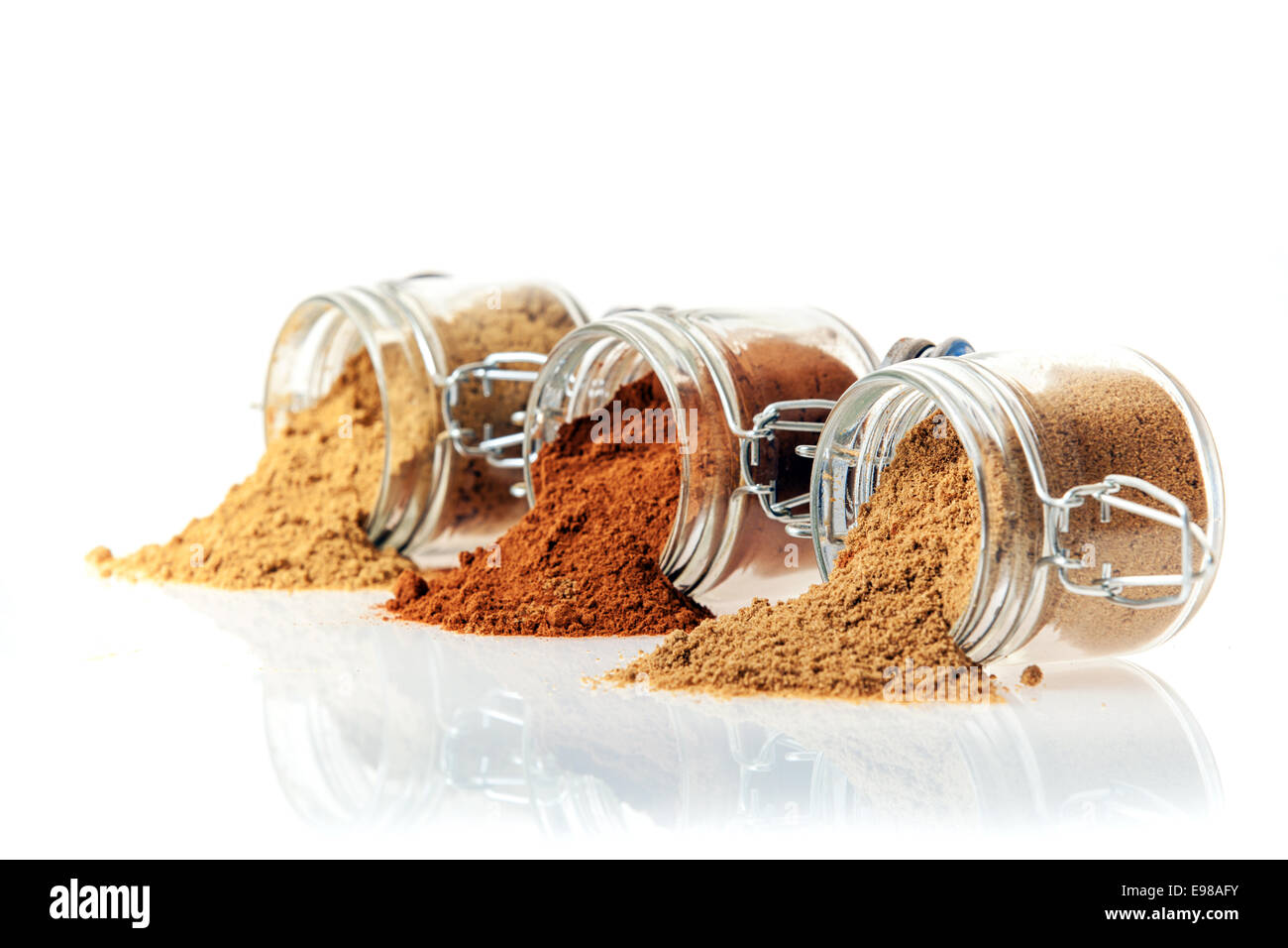 Three glass jars of ground spice lying on their side on a reflective white surface with their contents spilling out with copyspace Stock Photo