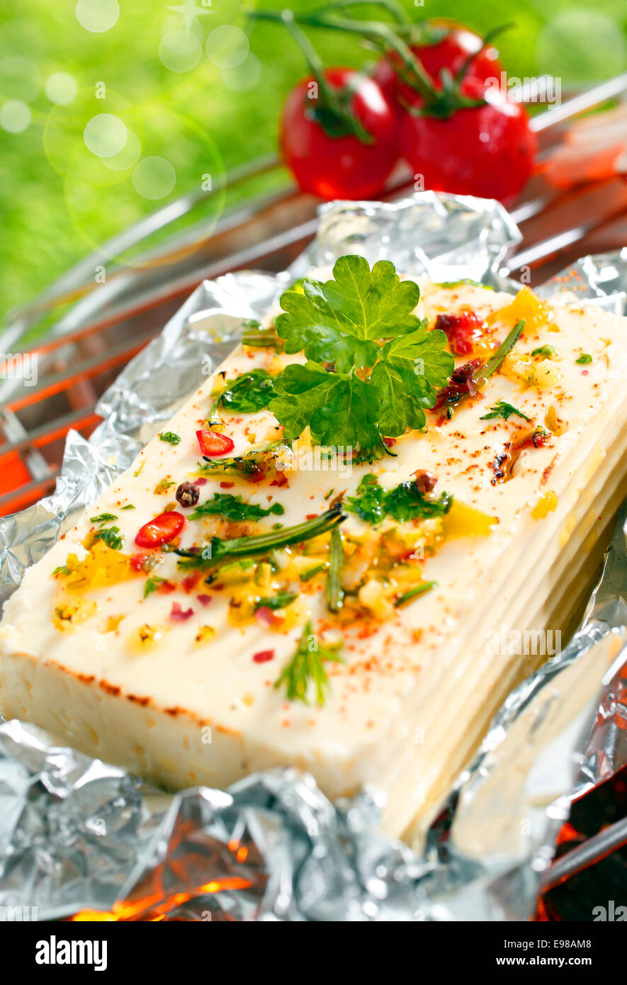 A delicious portion of feta cheese or halloumi topped with fresh herbs and spices grilling on an outdoor barbecue Stock Photo