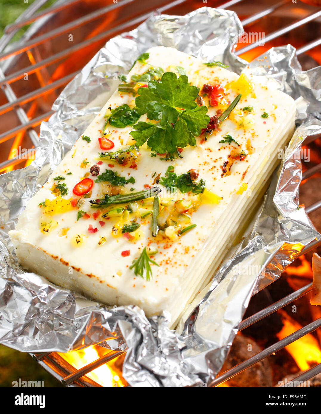 High angle view of a portion of feta or halloumi cheese topped with seasoning and spices grilling on a barbecue Stock Photo