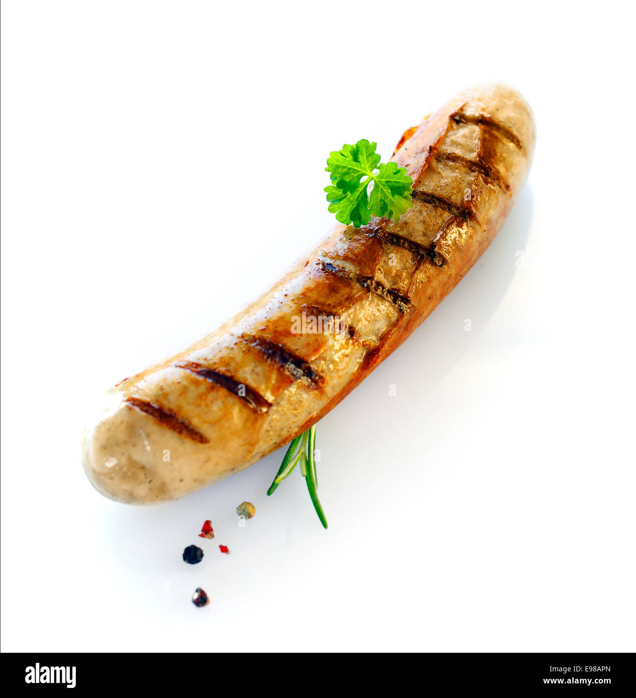 One cooked sausage with a sprig of parsley and rosemary shot against white. Stock Photo