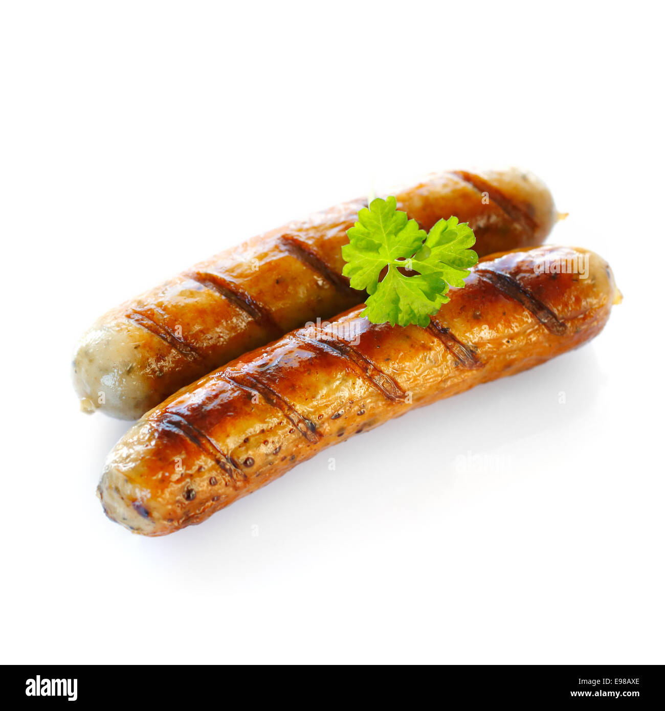 Close up of two cooked sausages, focus on the one at the front with a sprig of parsley on top against white background. Stock Photo
