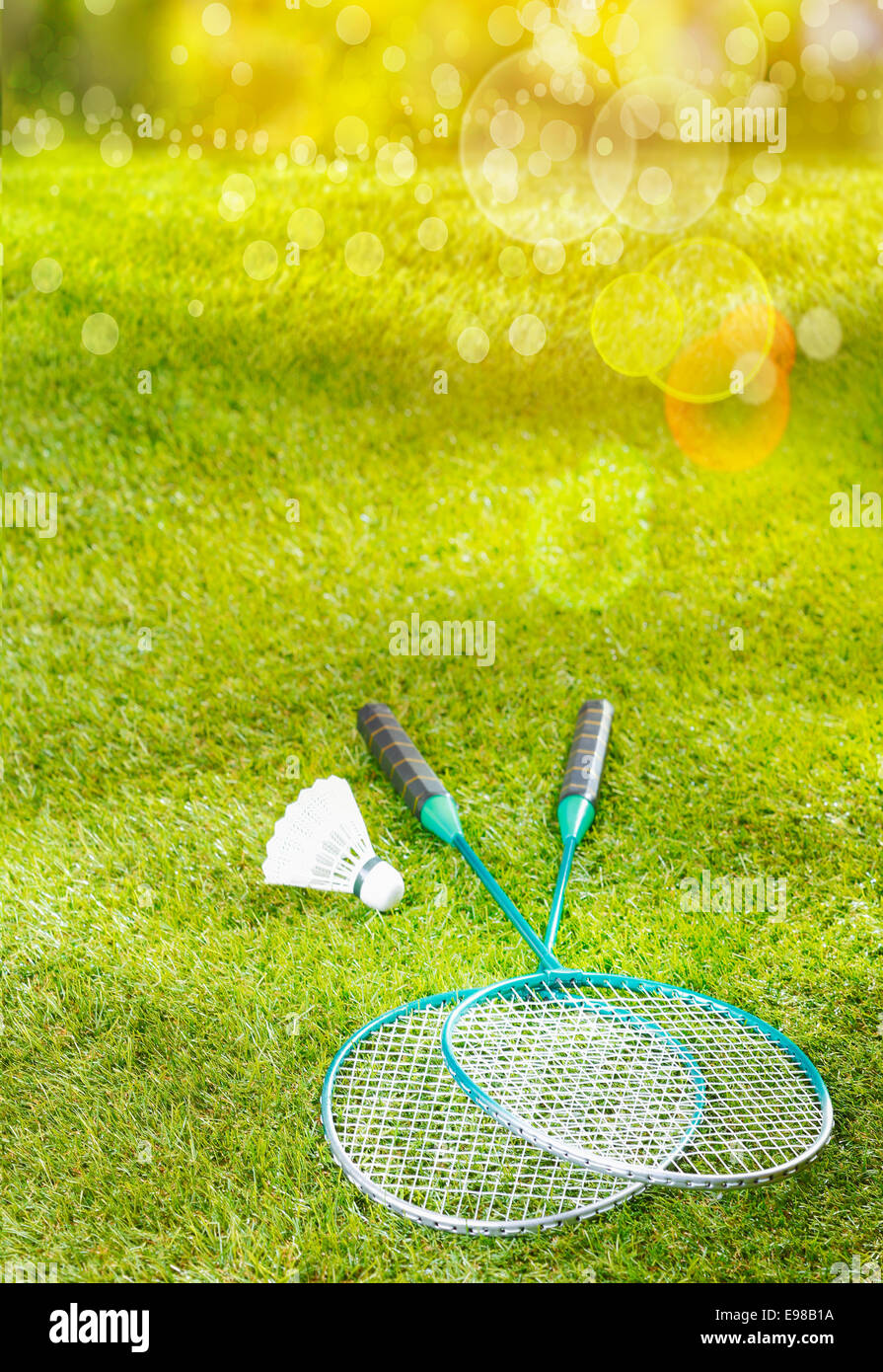 Badminton rackets and shuttlecock lying on a lush green lawn in warm golden summer sunlight with flare and bokeh Stock Photo