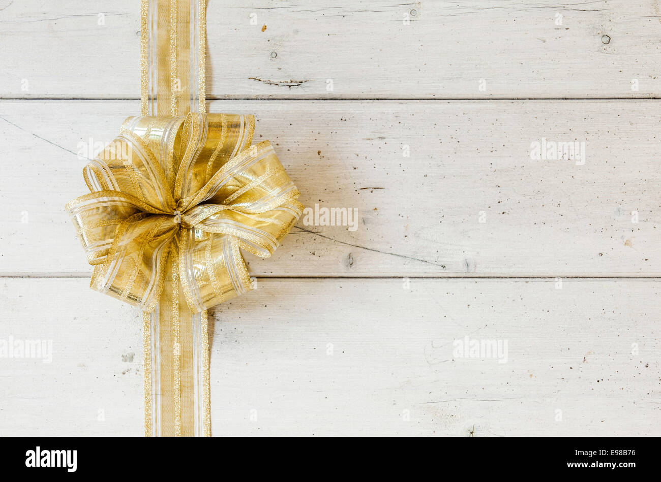 Metallic gold decorative Christmas bow forming a border on the left on a background of rustic white painted wooden planks with copyspace for your seasonal greeting Stock Photo