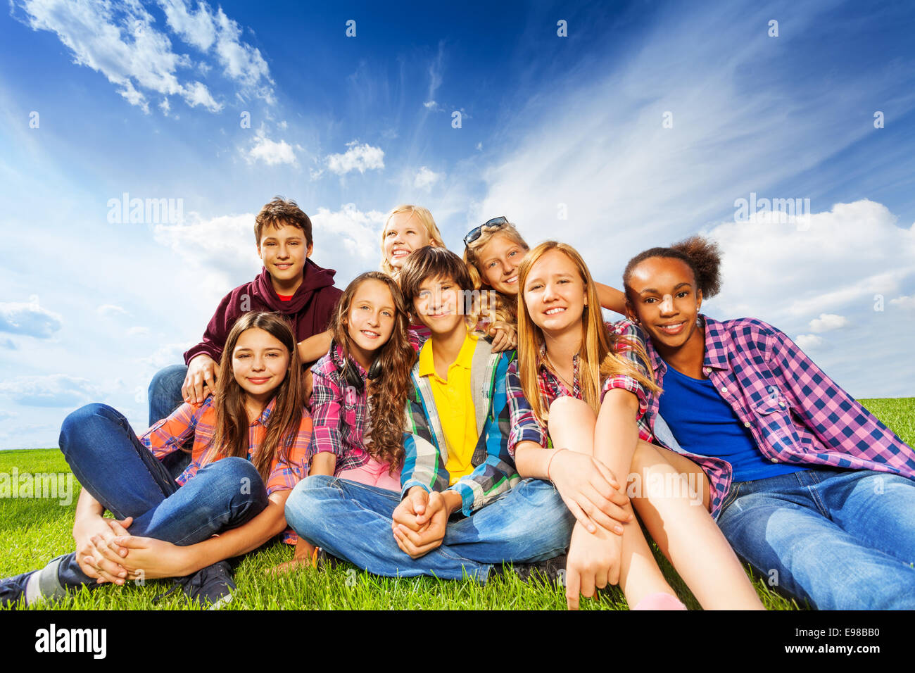 Happy friends sitting on green meadow Stock Photo