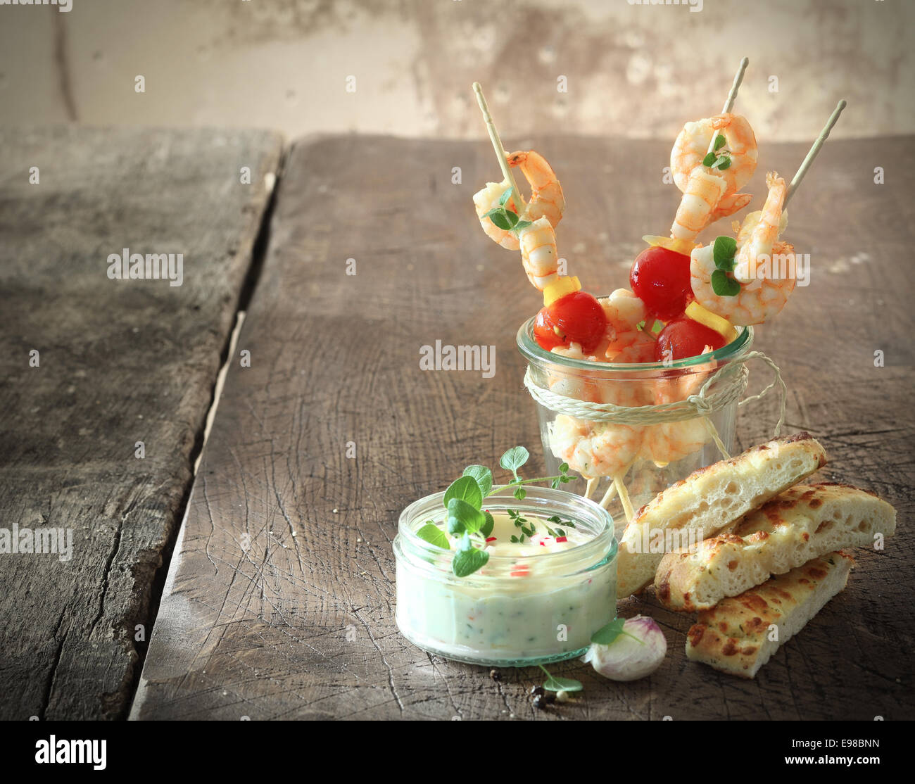 Tasty prawn or shrimp appetizers with tomatoes on skewers served with tartare sauce and fresh oven-baked Italian focaccia bread Stock Photo