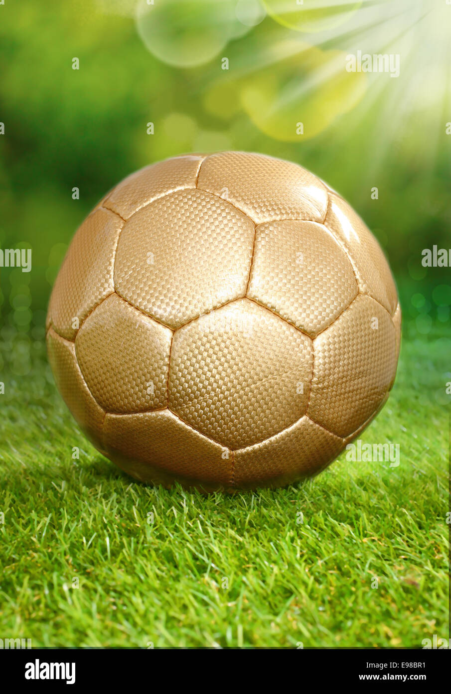 Conceptual image of a healthy outdoor lifestyle playing soccer in summer with a gold coloured soccer ball standing on lush green grass under the rays of the sun Stock Photo