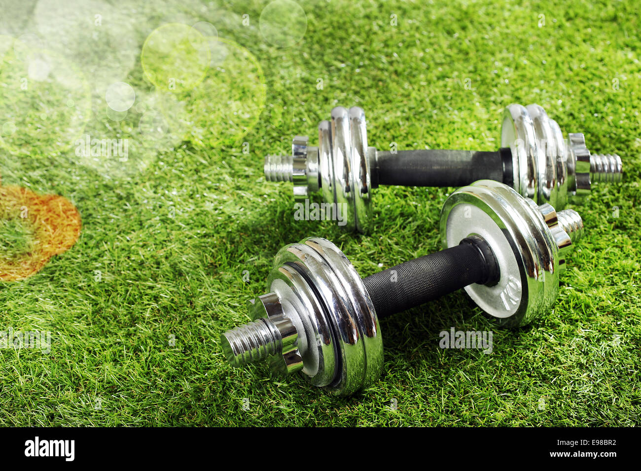 Metal dumbbells on green grass in summer sunshine with bokeh conceptual of fitness, exercise abd a healthy outdoor sporty lifestyle Stock Photo