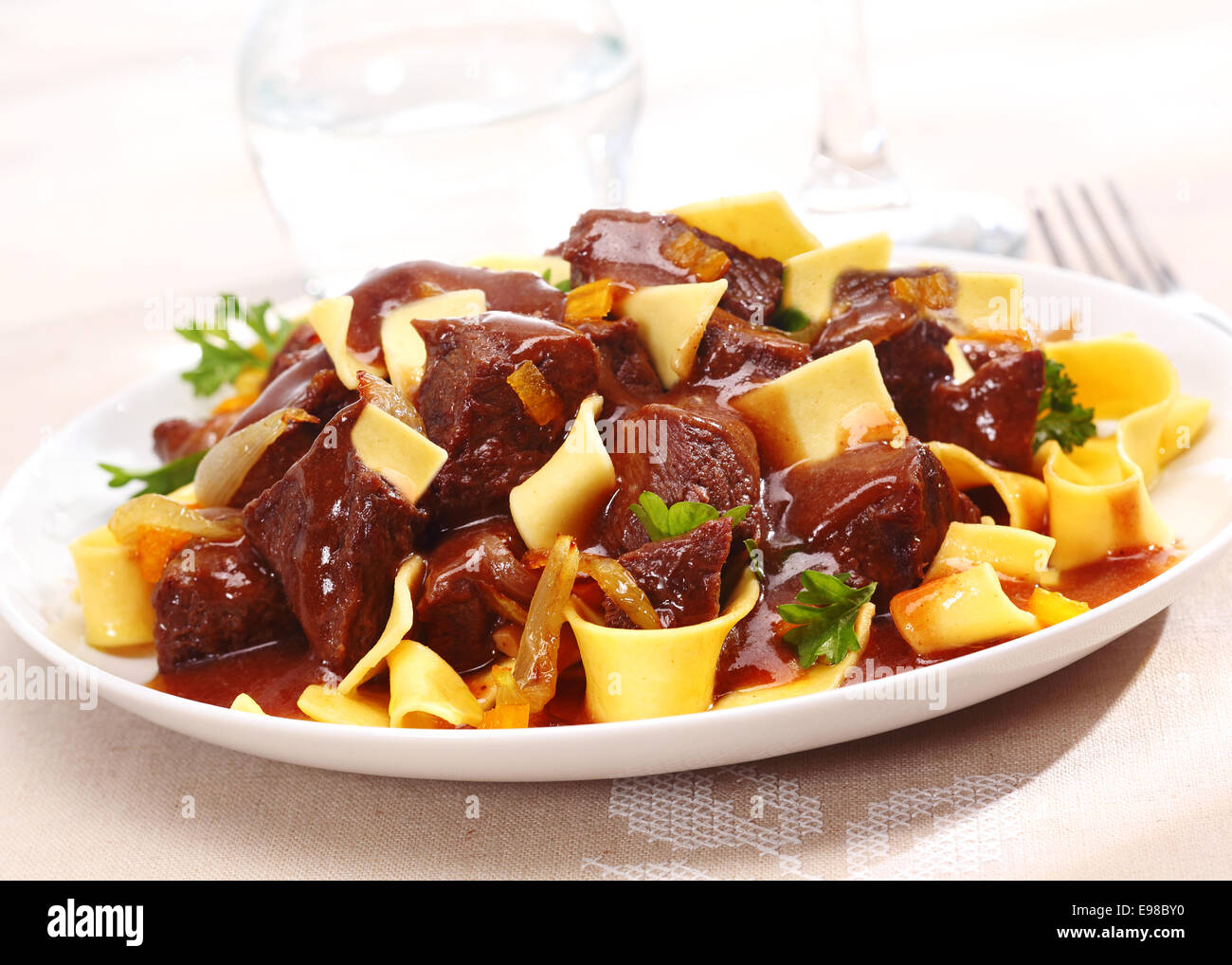 Serving of braised beef goulash in a rich brown gravy sauce on pasta or