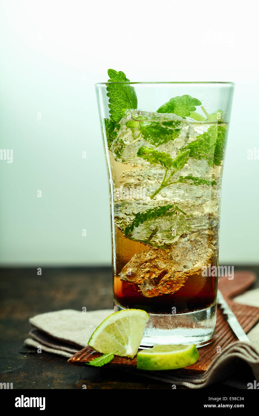 A tall glass of ice cold mujito rum cocktail with mint leaves and lime standing on a folded napkin and coaster on a wooden counter in a bar or club Stock Photo