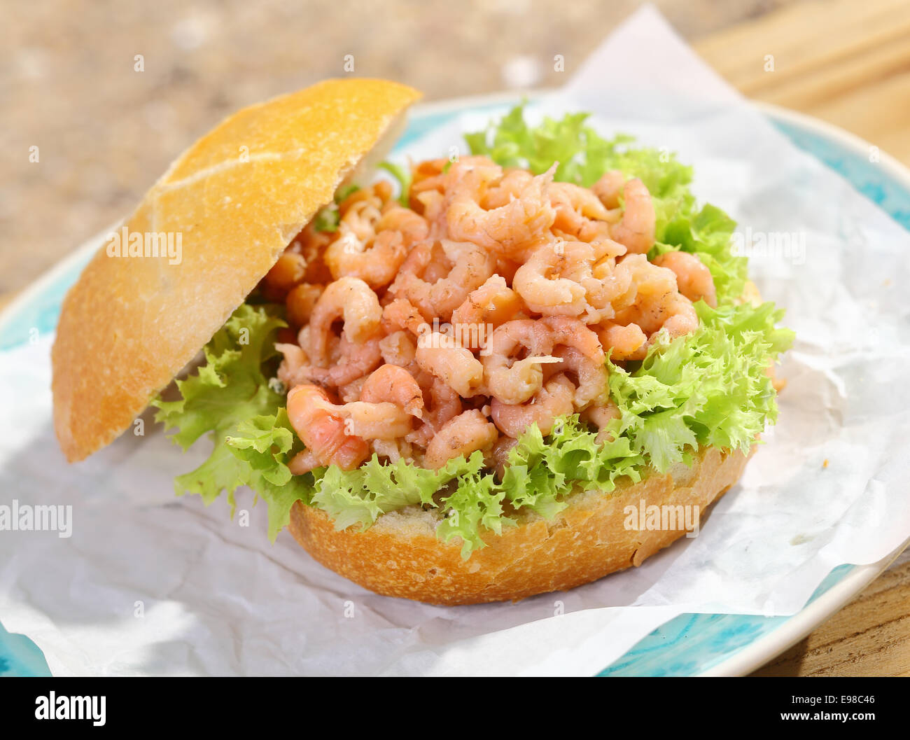 Delicious fresh crisp crusty roll with frilly lettuce topped with shrimp filling served on a napkin on a plate for a gourmet seafood lunch Stock Photo