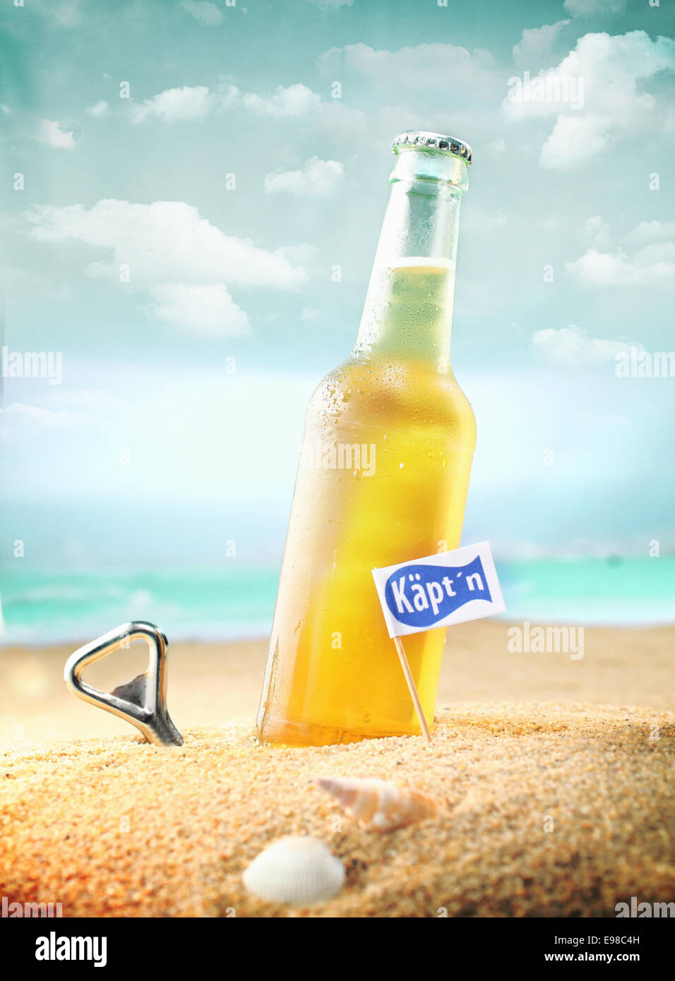 Beautiful photo of a chilled beer and a bottle opener on the beach tagged as Kapt'n. Stock Photo