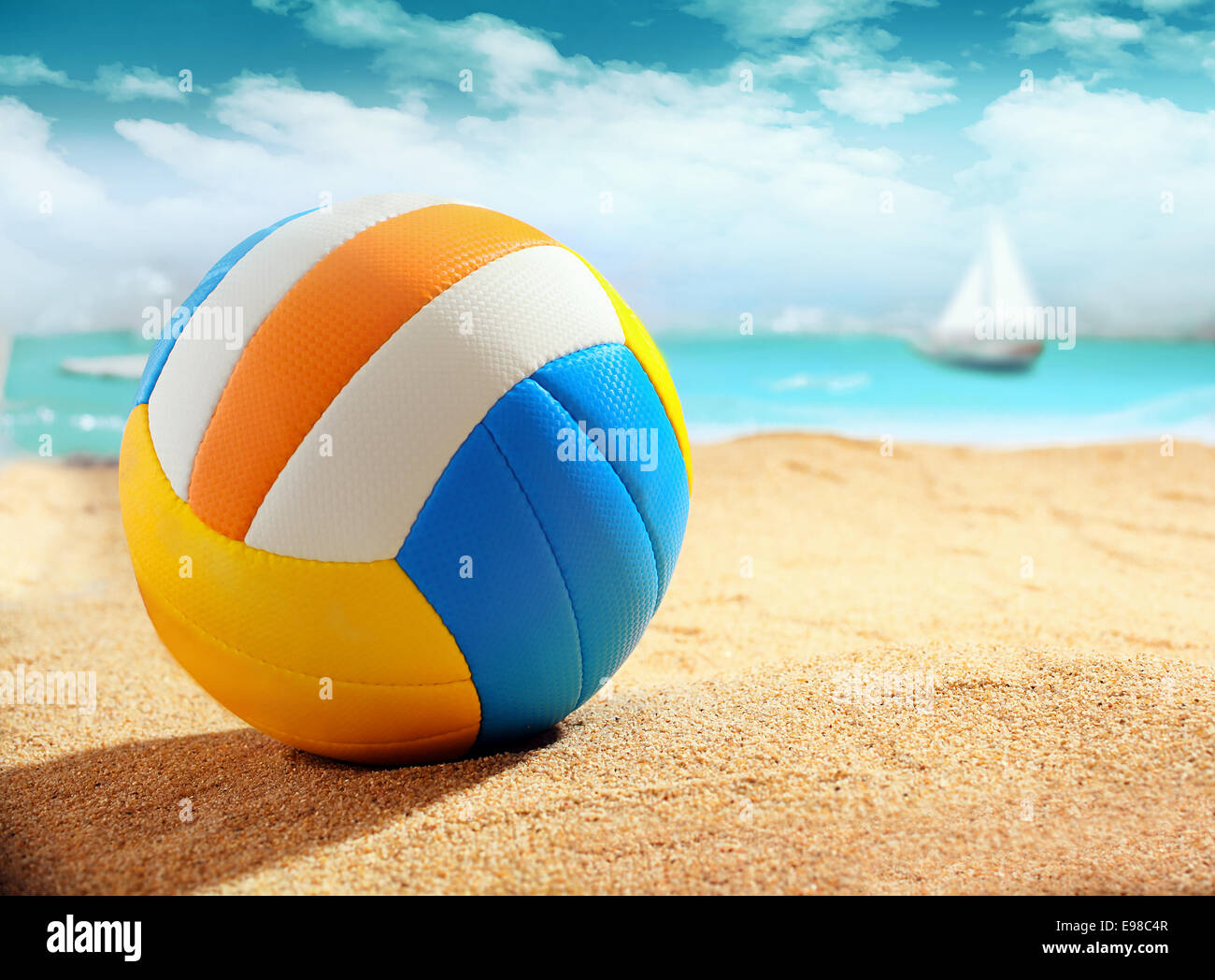 Colourful beach ball on the golden sand of a tropical beach with the ocean and a yacht visible behind, shallow dof Stock Photo