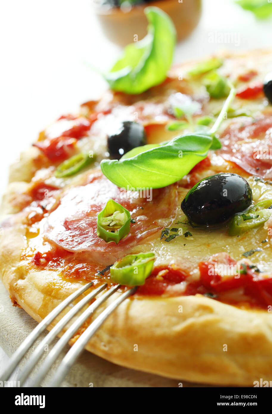 Closeup of crusty homebaked salami pizza with tomatoes, cheese, basil and sliced chilli peppers for delicious Italian cuisine Stock Photo