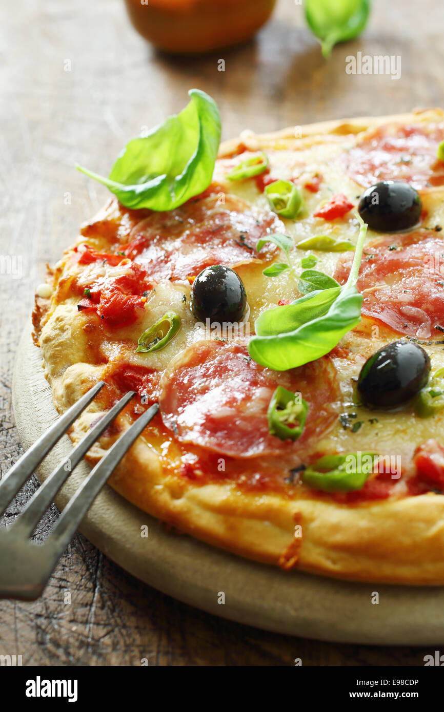 Savoury Italian salami pizza on a crisp golden crust with basil, chilli pepper, olives and cheese on tomato paste served on an old rustic wooden board. More pizza at my port. Stock Photo