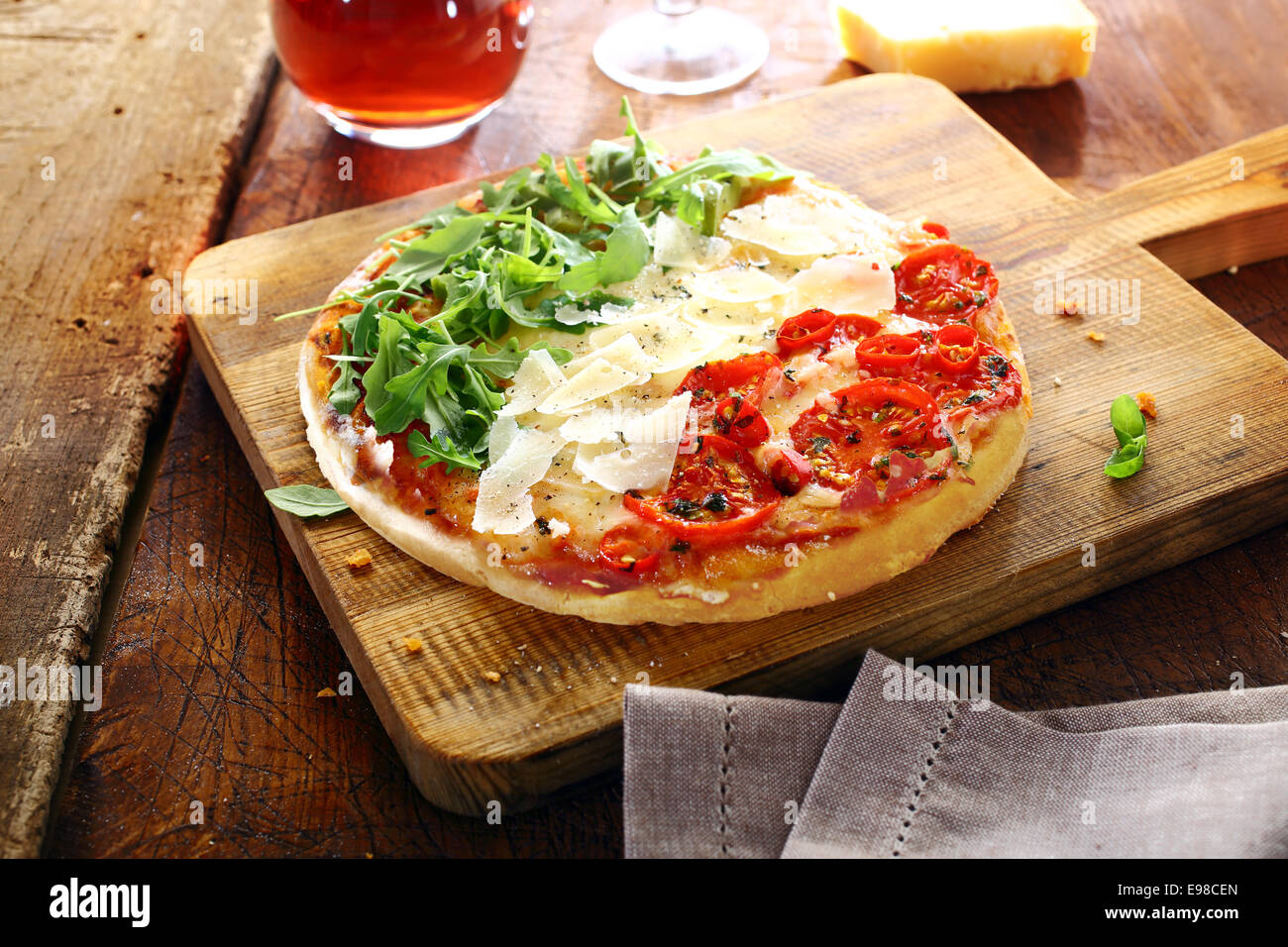 Colourful Italian pizza in the national colours topped with fresh green rocket leaves, white shavings of cheese and red tomatoes in three stripes standing on a wooden board on an old rustic table Stock Photo