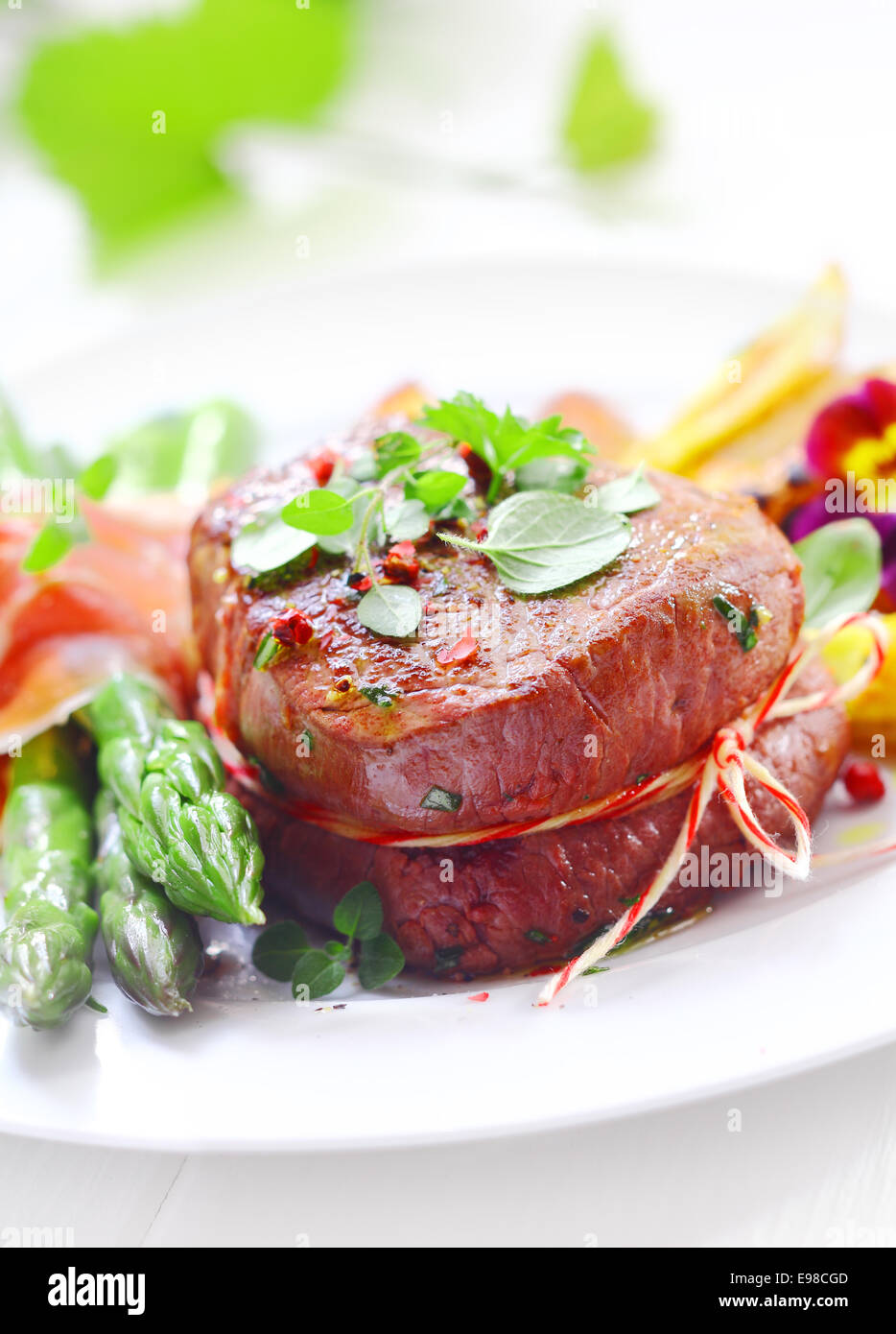 Succulent tender fillet steak medallion tied with string and served with fresh green asparagus spears wrapped in thinly sliced ham or bacon Stock Photo
