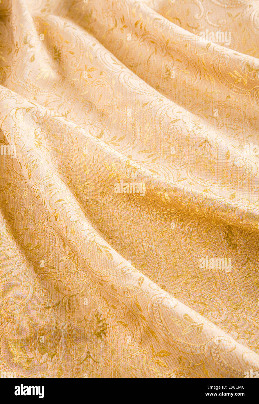 Soft luxuriant folds of gold damask fabric with a shiny embroidered pattern of acanthus leaves and flowers for a stylish interior decoration Stock Photo