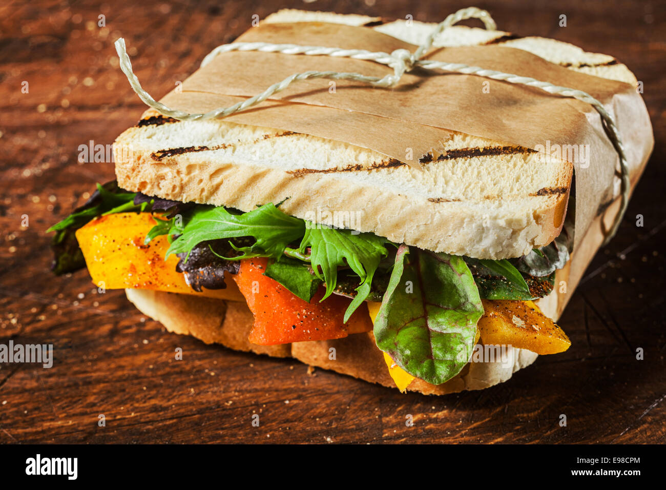 Takeaway grilled toasted sandwich with pepper,cheese,rocket, spinach and leafy green herbs tied with a brown paper wrapper and string Stock Photo