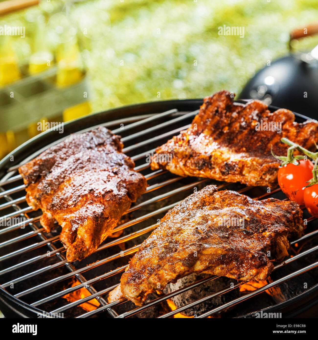 Close up of three portions of marinated seasoned rib grilling on a portable BBQ during a summer picnic or camping trip Stock Photo