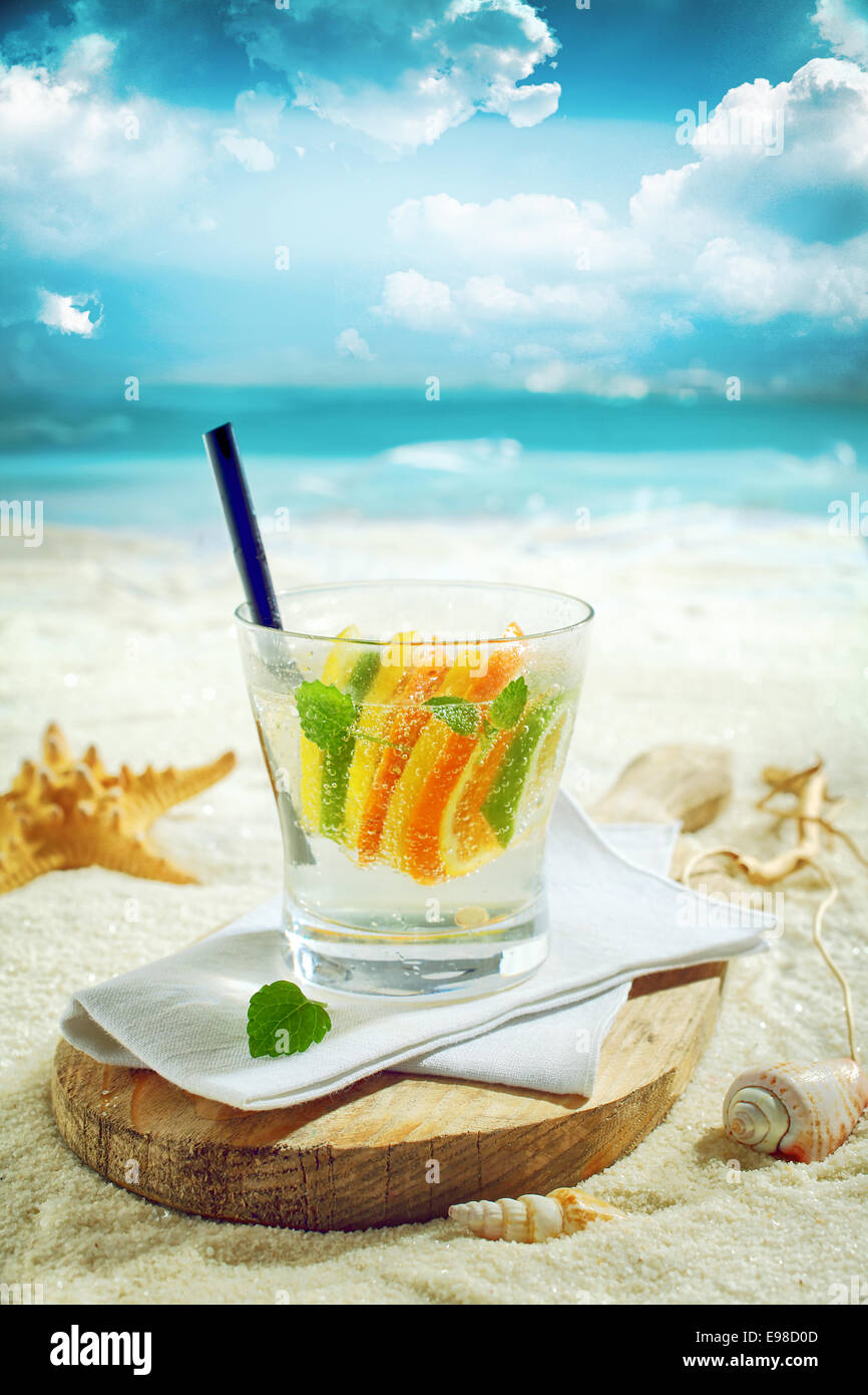 Delicious gin or vodka citrus cocktail served on a sunny tropical beach on a rustic wooden board with ocean backdrop Stock Photo