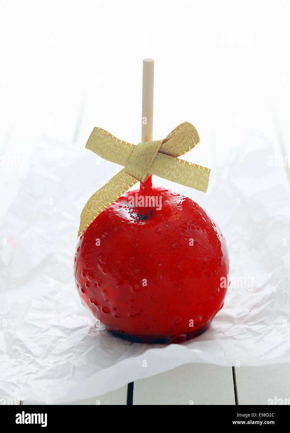 Festive colourful red toffee apple with a bow covered in hard sugary candy syrup for a holiday celebration Stock Photo
