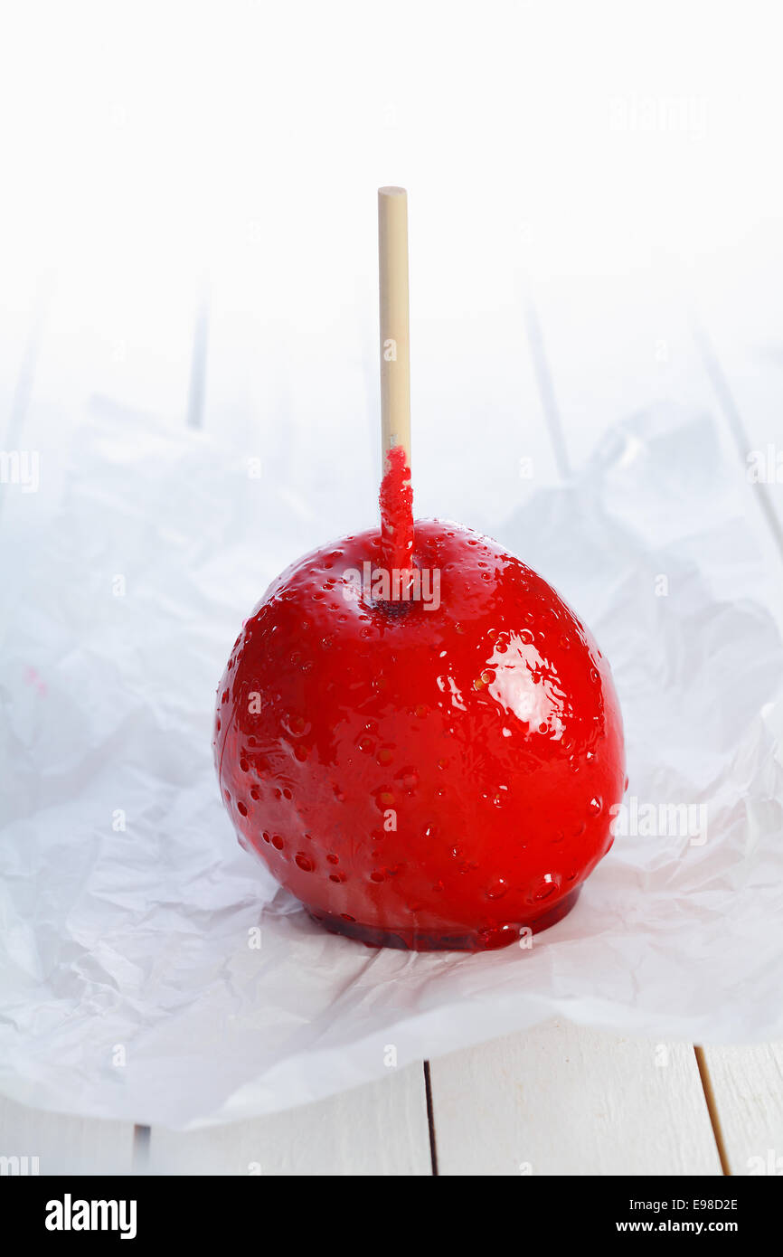 Colourful toffee apple on a stick covered in hard red sugar candy standing on crumpled paper to be served as a festive treat Stock Photo