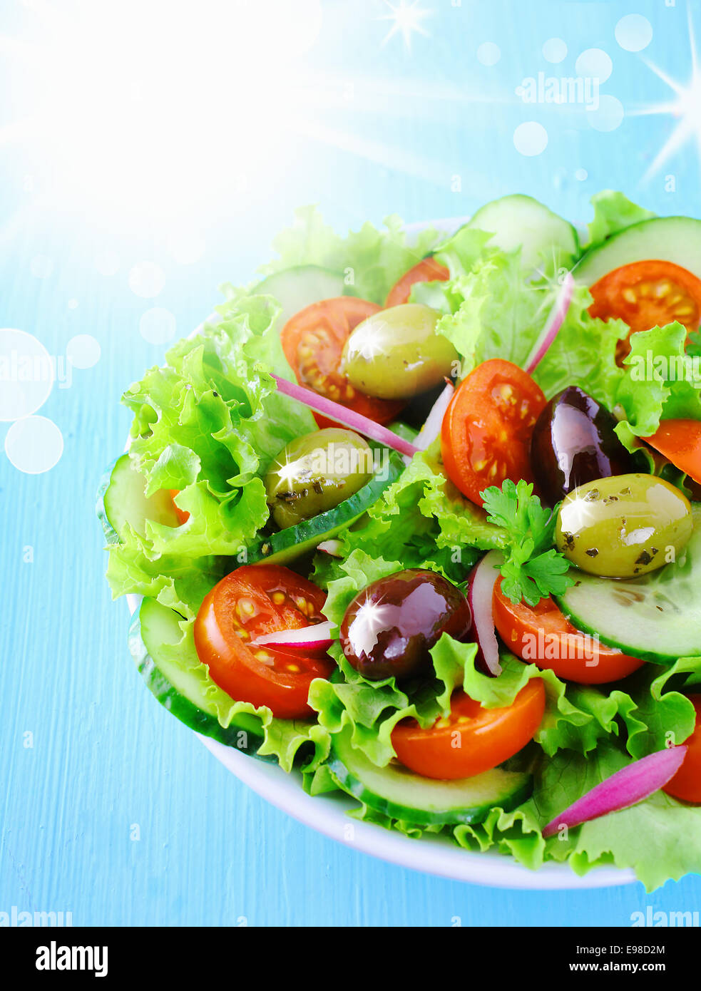 Fresh leafy green summer salad with tomato and olives under a hot sun with flare andd bokeh Stock Photo