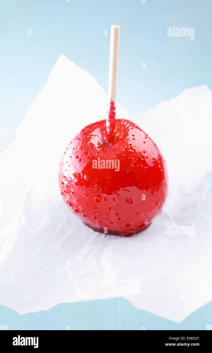 Delicious childhood candy or taffy apple coated in a colourful hard red sugar syrup standing on crumpled white paper Stock Photo