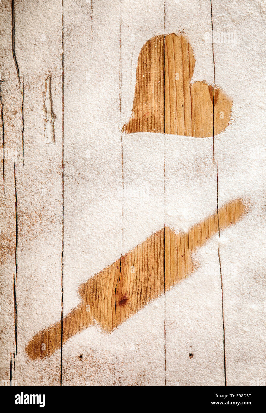 Imprint of a heart and rolling pin in flour on a wooden table top depicting a love of baking and cooking or as a romantic message on Valentines Day Stock Photo