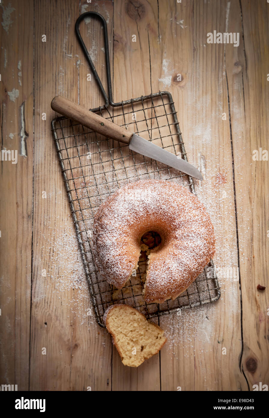 Overhead view of a slice cut from a freshly baked ring cake cooling on a wire rack in a country kitchen on an old wooden table Stock Photo